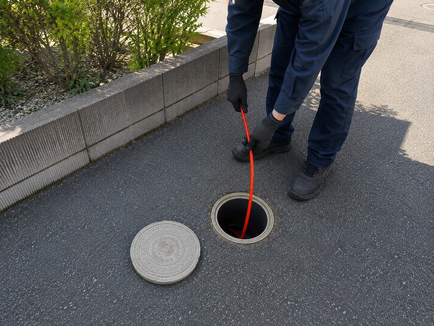 戸建て住宅の屋外排水桝から洗浄ホースを通す作業スタッフ